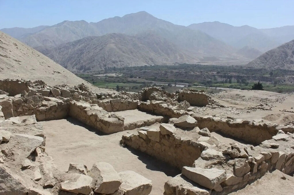 Ruinas de piedra del sitio arqueológico de Incahuasi en el valle de Cañete, con el paisaje árido y los cultivos al fondo