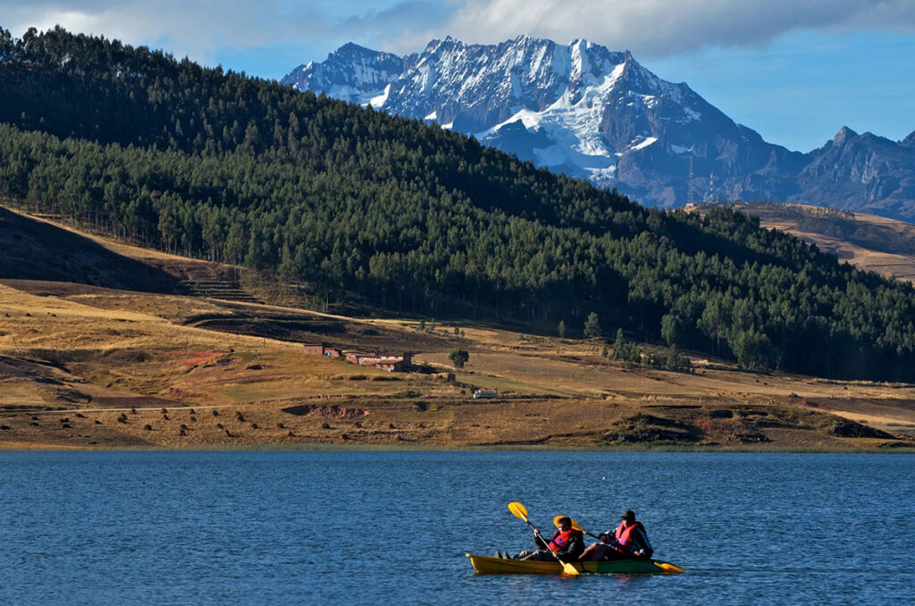 Vista de la laguna Huaypo con montañas nevadas al fondo y dos visitantes navegando en bote en el Valle Sagrado del Cusco