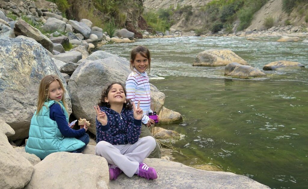 Niños sentados junto al río en Lunahuaná durante una salida familiar