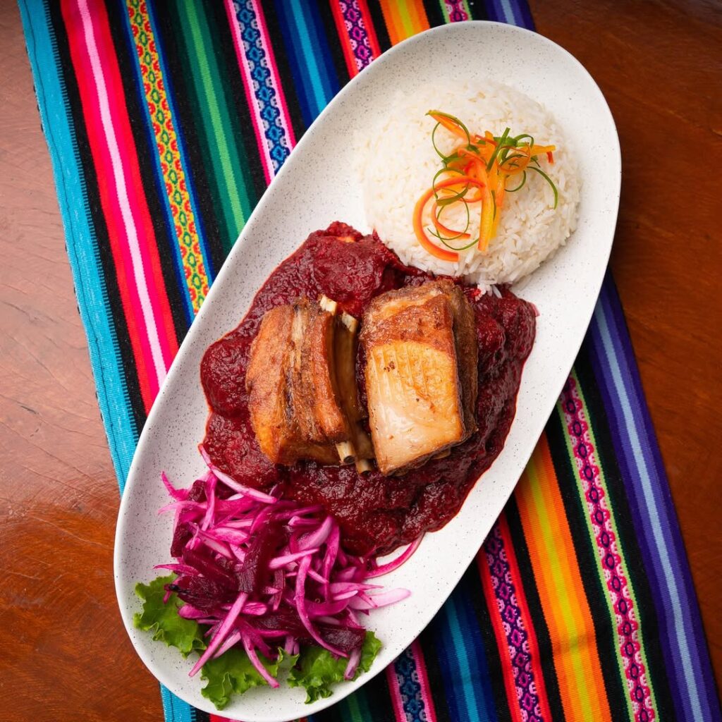 Plato tradicional de Puca Picante servido con arroz y ensalada, sobre mantel andino colorido típico de Ayacucho