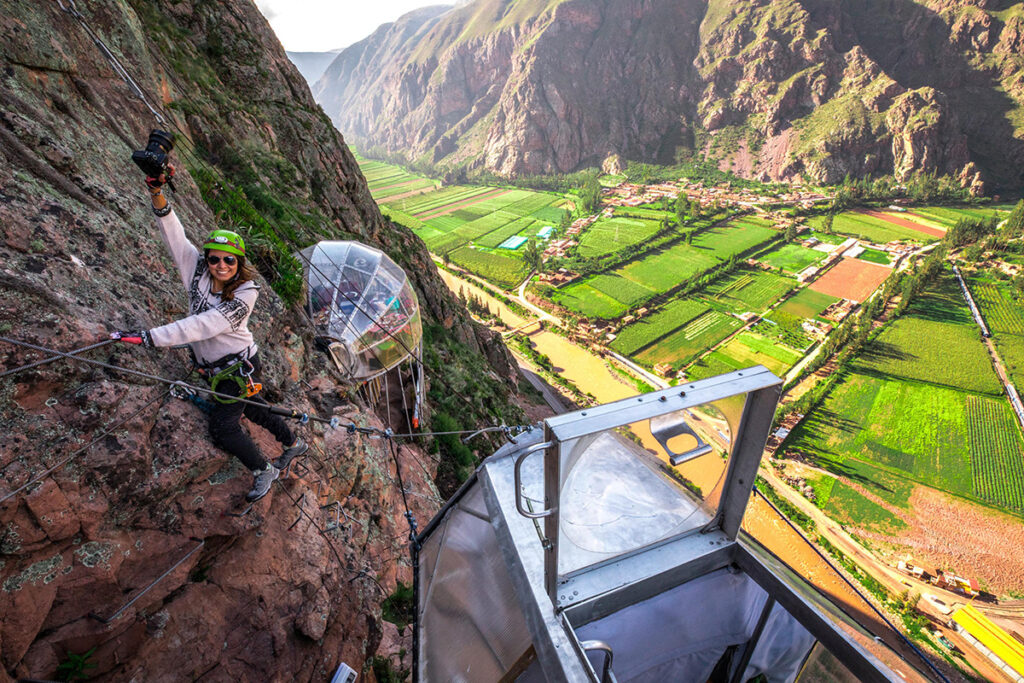 Turista ascendiendo por la vía ferrata de Skylodge con vista al Valle Sagrado desde la pared rocosa.