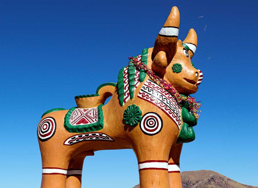 Torito de Pucará de gran tamaño decorado con motivos geométricos y florales en tonos blanco, verde y rojo, colocado en un espacio abierto bajo un cielo azul