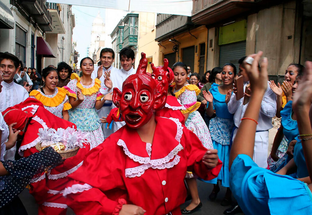 Danzante con máscara roja durante una celebración cultural en El Carmen, Chincha, acompañado por músicos y pobladores locales