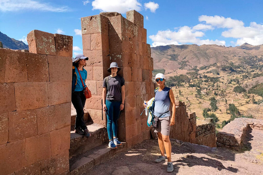 Visitantes junto a muros de piedra en el sector alto de Pisac, con vistas amplias del valle y montañas en el fondo