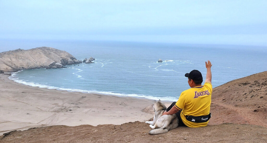 Persona y perro descansando en la cima del Morro Solar, con vista amplia a la costa de Lima y acantilados del Pacífico