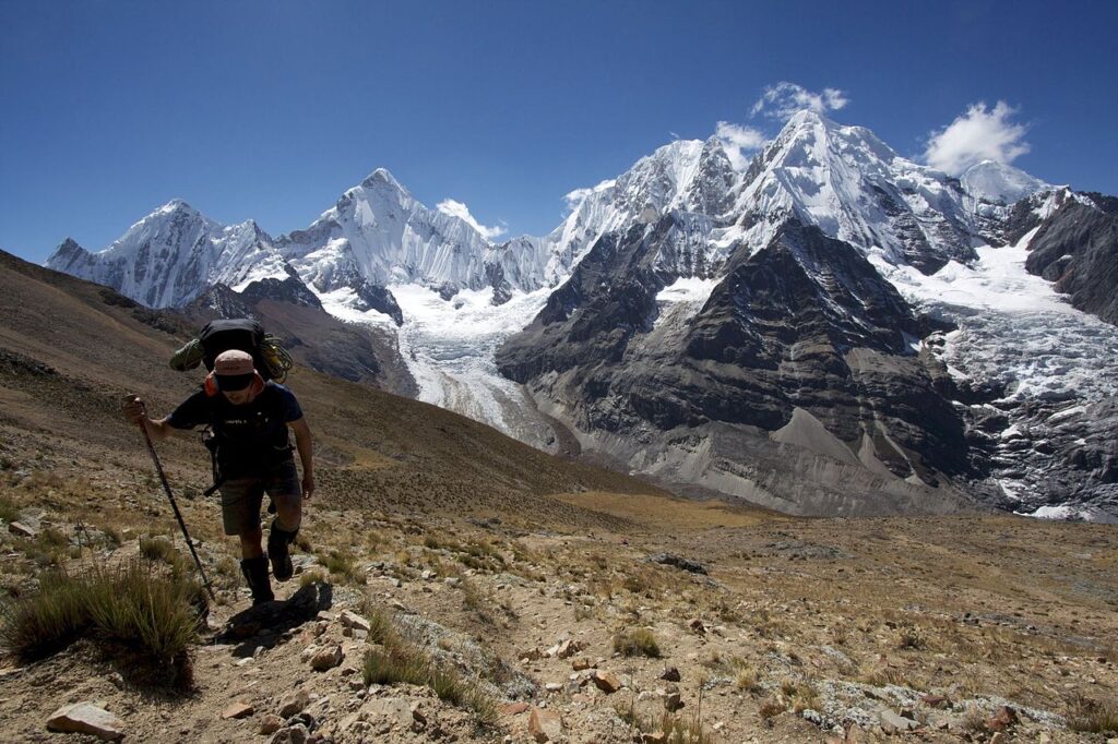 Trekker avanzando por la Cordillera Huayhuash con cumbres nevadas de más de 6.000 metros dominando el recorrido