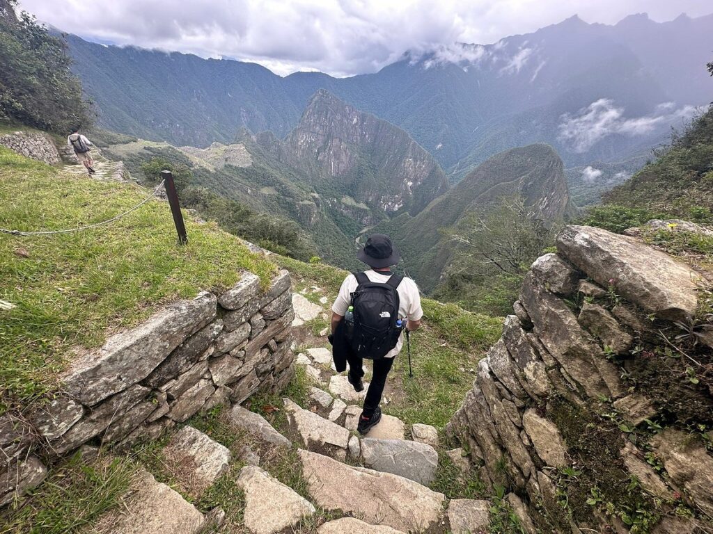 Visitante descendiendo por el sendero hacia Intipunku con vista al valle y montañas de Machu Picchu