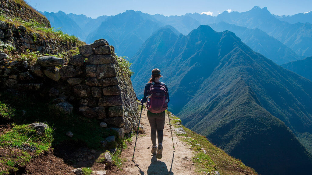Senderista caminando hacia Intipunku con vistas abiertas al valle y las montañas de Machu Picchu