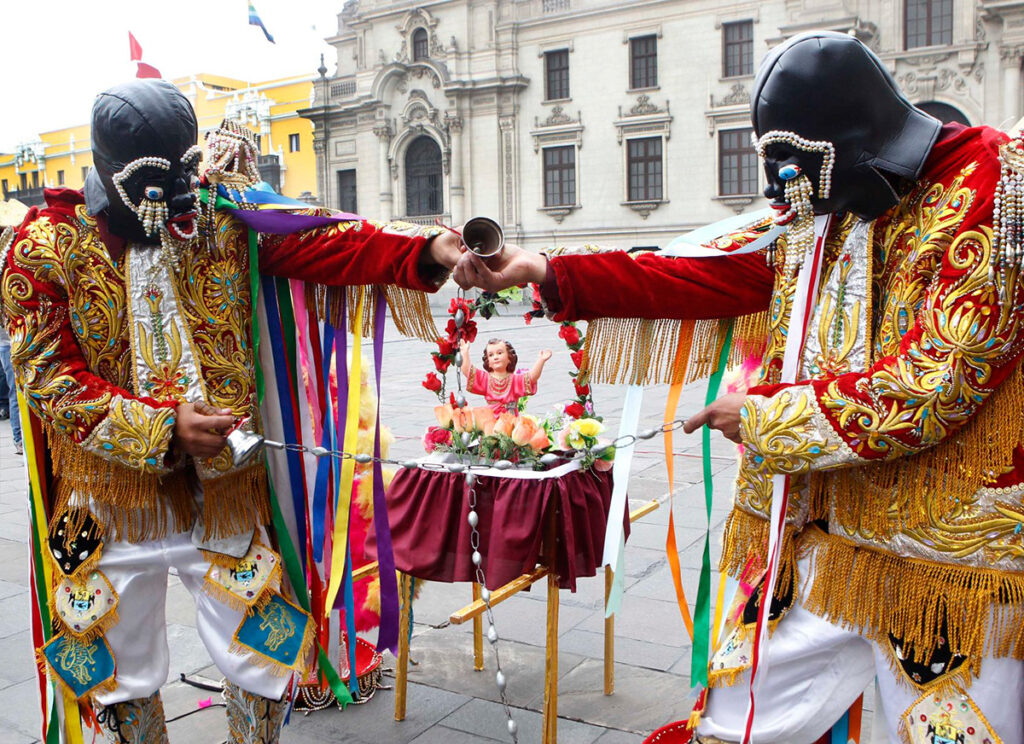 Danzantes de los Negritos de Huánuco realizan una ofrenda al Niño Jesús durante la celebración navideña, con vestimenta tradicional y máscaras rituales en un espacio urbano histórico