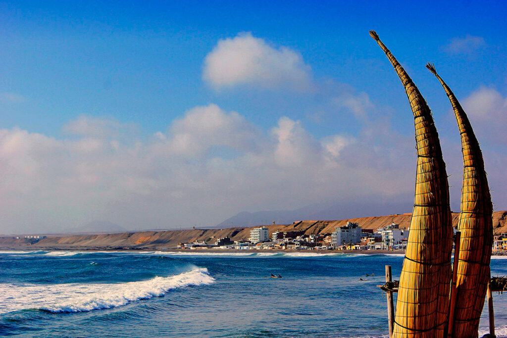 Playa de Huanchaco al amanecer, con caballitos de totora frente al mar y el balneario al fondo, en la costa norte del Perú