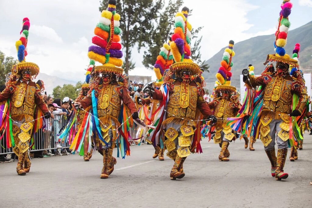 Cuadrilla de danzantes de los Negritos de Huánuco avanzando en formación durante la festividad, con vestimenta ritual, máscaras tradicionales y acompañamiento musical en espacio urbano